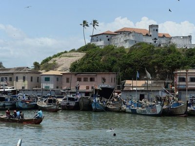 Vissersboten in de haven van Elmina met Fort Elmina op de heuvel, Ghana.