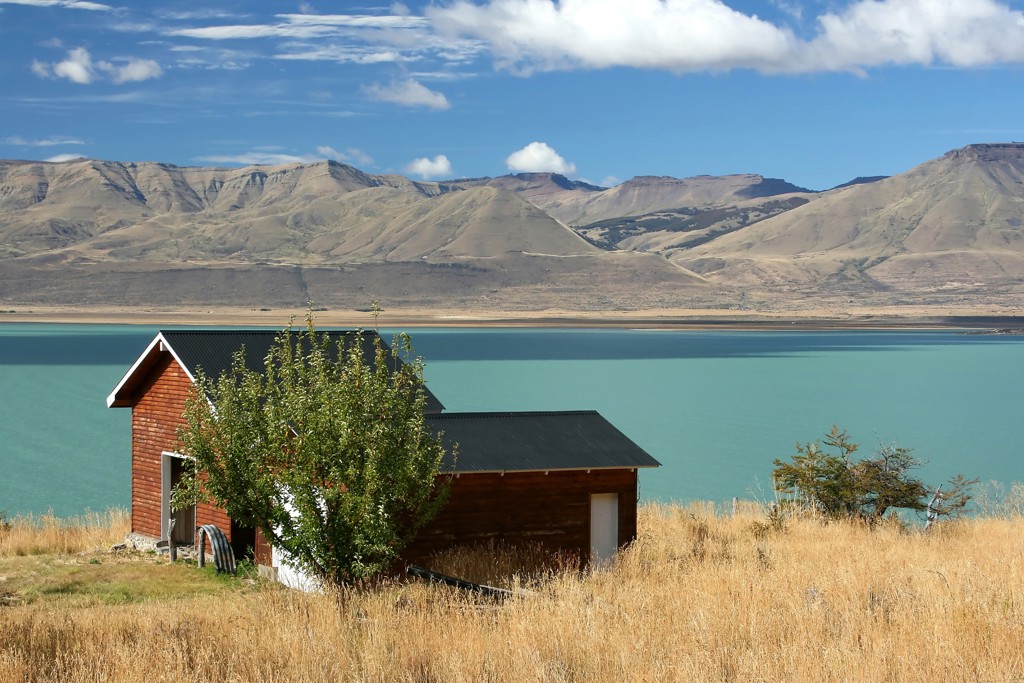 Huisje aan een turkoois meer met bergen op de achtergrond in Argentinië tijdens een groepsrondreis.