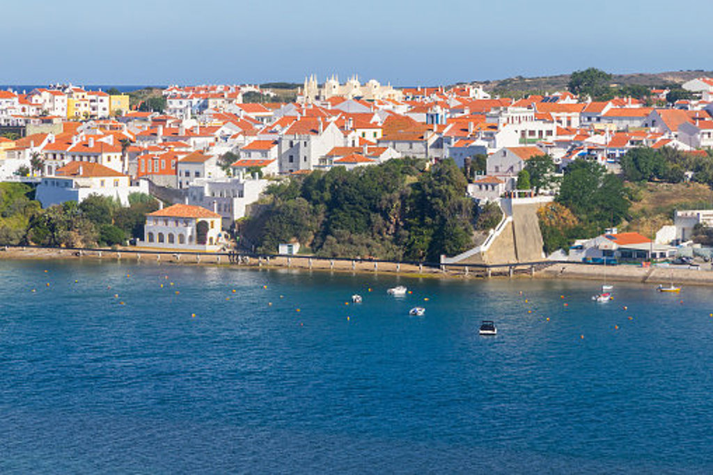 Zicht op een kustplaats aan de Costa Vicentina in Portugal met witte huizen, rode daken en een haven.