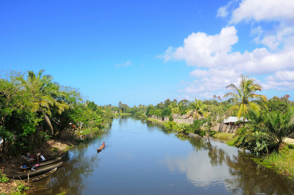 Rivierlandschap in Madagascar met kano’s, palmbomen en dorpjes langs de oevers onder een blauwe lucht.