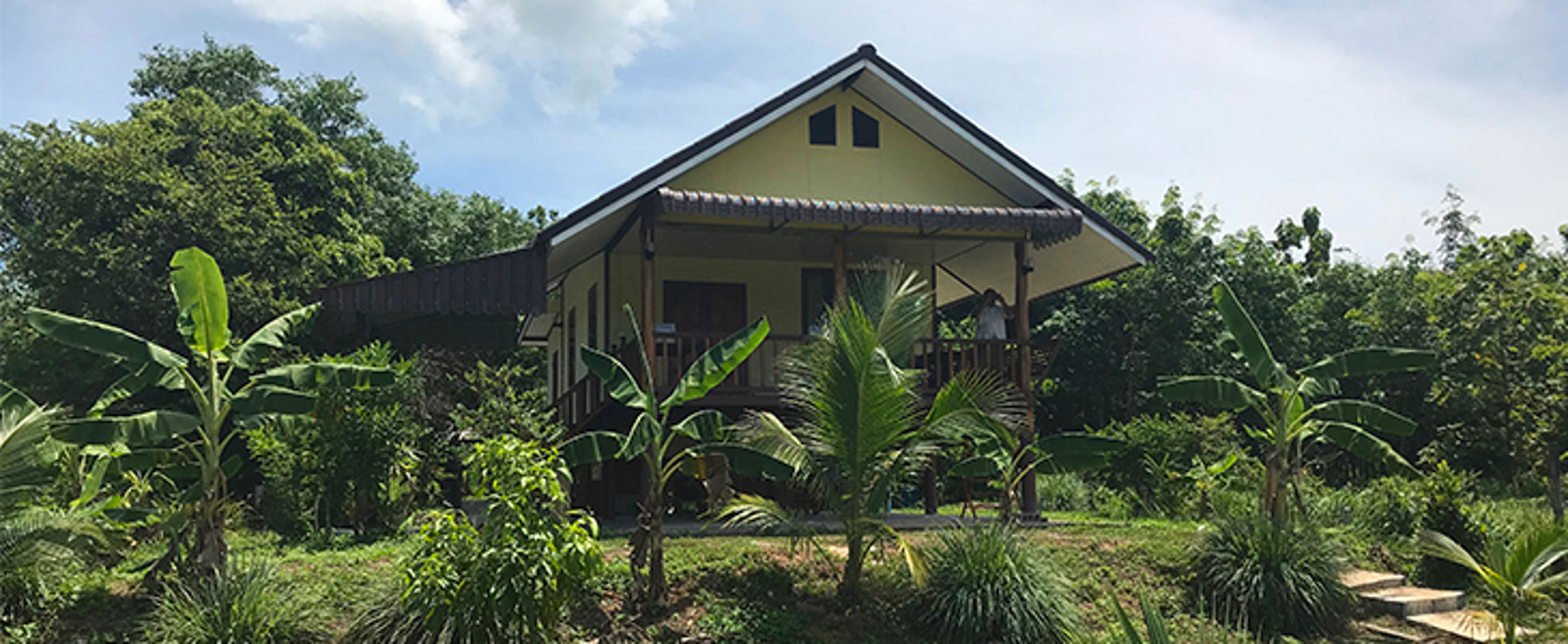 Homestay in Azië Houten bungalow met veranda tussen tropisch groen en palmbomen.