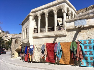 Traditioneel stenen gebouw in Cappadocië met kleurrijke tapijten en doeken langs de muur.