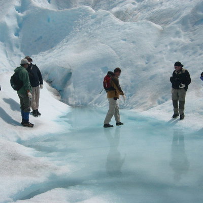 Wandelaars op een gletsjer met azuurblauw smeltwater tijdens een groepsrondreis Patagonië.