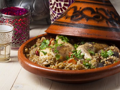 Marokkaanse tajine met kip, groenten en kruiden, geserveerd in een aardewerken schaal.
