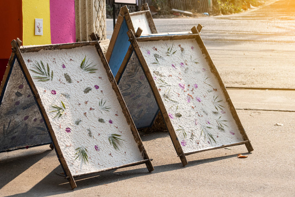 Handgeschept papier met bloemen en bladeren droogt in houten frames tijdens familiereis Thailand, Laos en Cambodja.