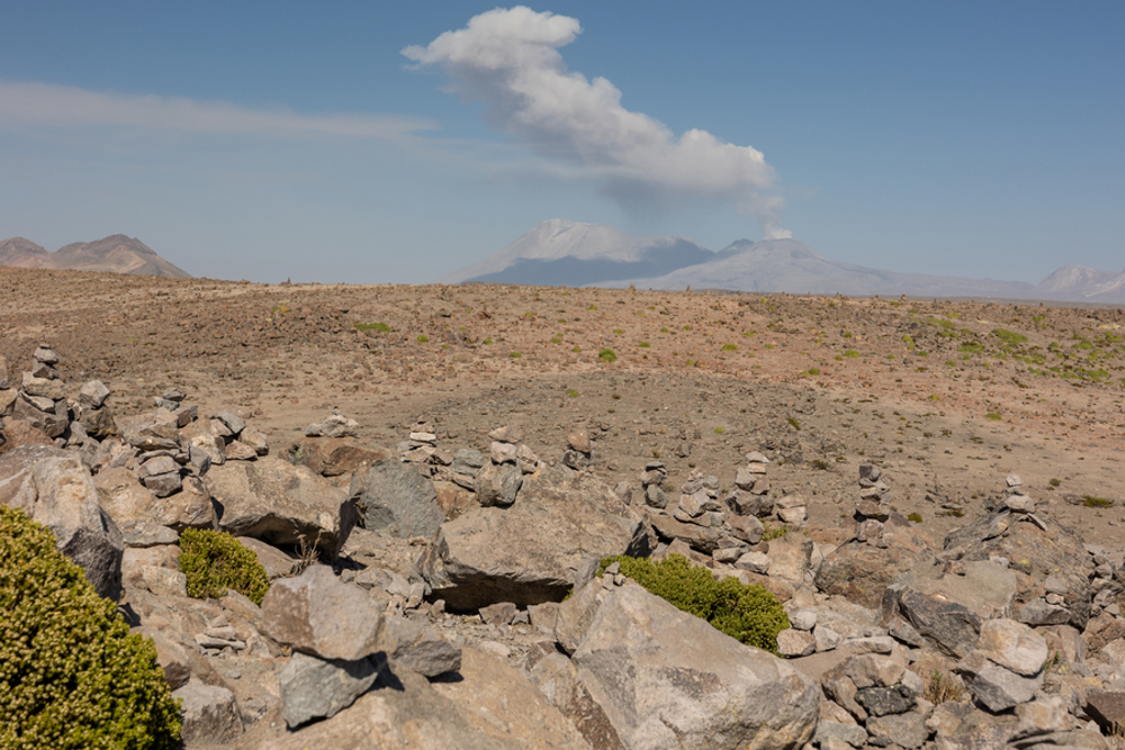 Rotsachtig hooglandlandschap in Peru met rookpluim van een vulkaan onder een blauwe lucht.