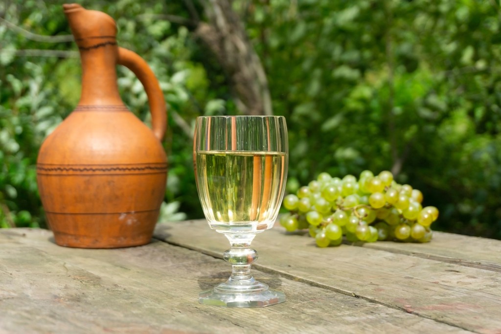 Glas Georgische wijn met druiven en aardewerken kruik op houten tafel.