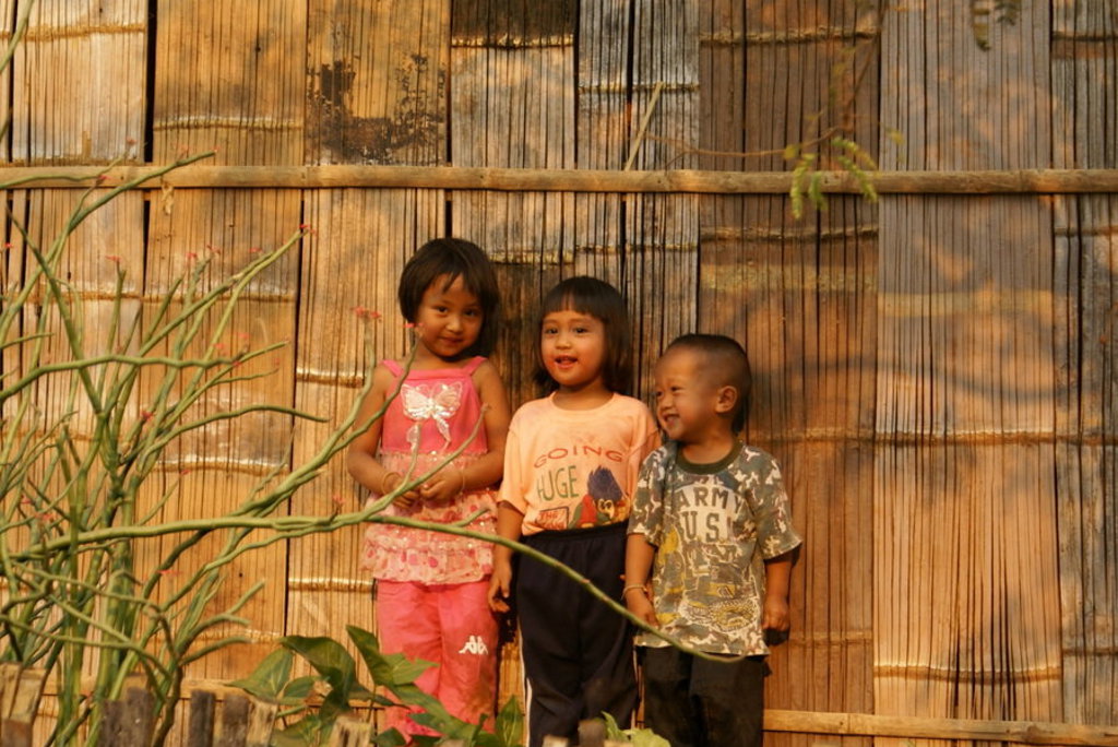 Drie kinderen poseren lachend voor een bamboewand tijdens een groepsrondreis Thailand.