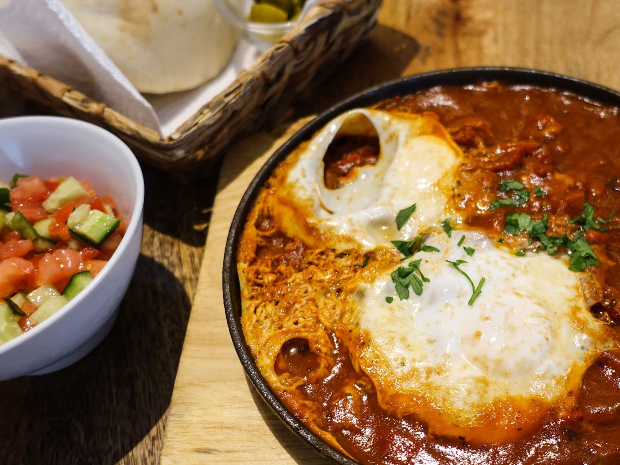 Shakshuka met gepocheerde eieren in tomatensaus, geserveerd met salade en brood.