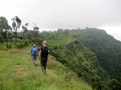 Wandelaars met rugzak lopen langs groene heuvels en terrassen tijdens de Route Nepal Familiereis 15 dagen, .