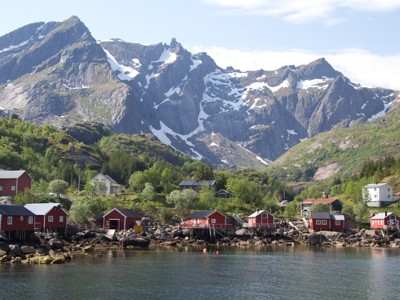 Rode vissershuisjes aan een fjord met ruige bergen en sneeuwvelden op de achtergrond, Noorwegen.