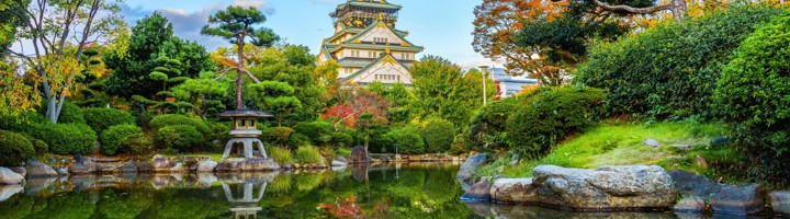 Osaka Castle met weerspiegeling in een vijver, omringd door een Japanse tuin.