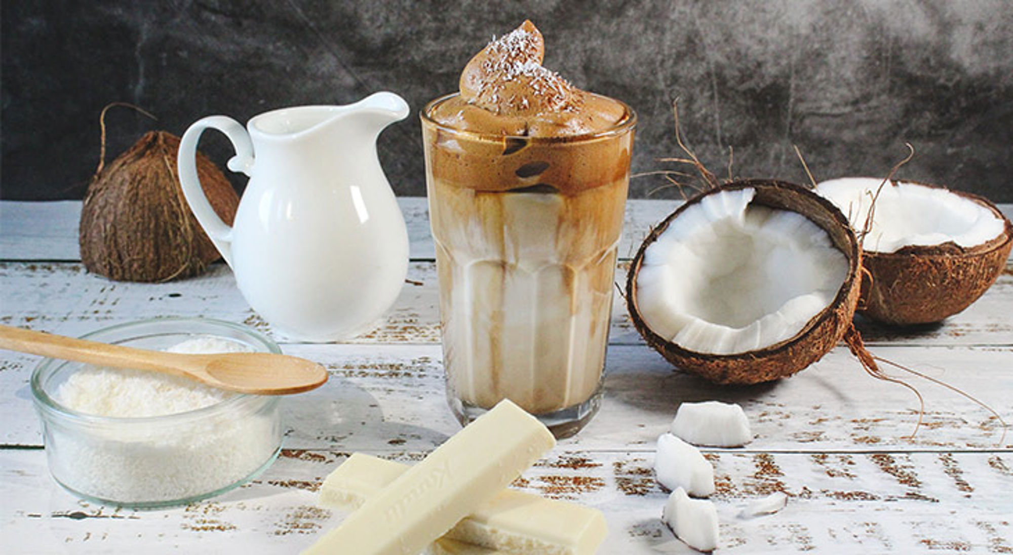 Iced koffie met kokosmelk en chocolade, omringd door kokosnoten en kokosrasp.