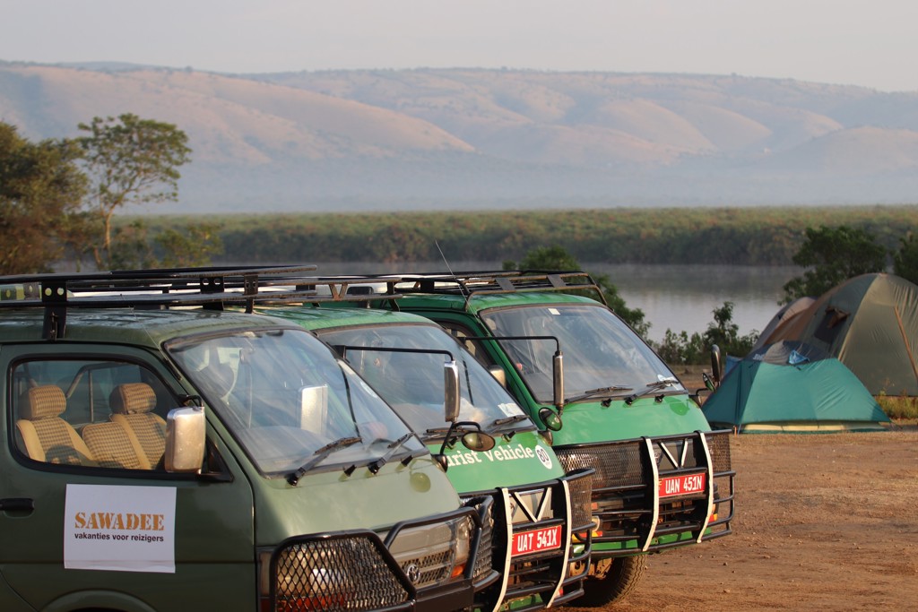 Safariwagens en tenten bij een rivier in Oeganda tijdens de groepsrondreis Oeganda Natuur Plus Pop-Up.