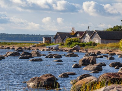 Houten vissershuisjes aan de rotsachtige kust van de Baltische Staten, met boten en ondiep water.