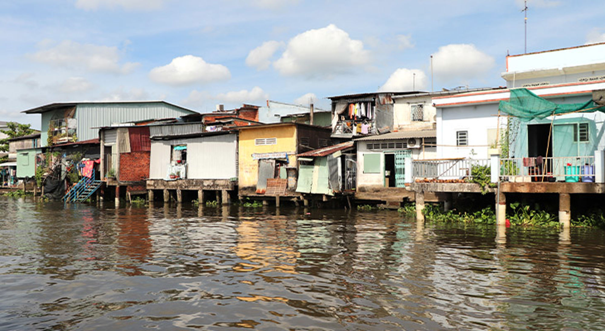 Mekong Delta Huizen op palen langs het water, met kleurrijke gevels en wasgoed onder een blauwe lucht.