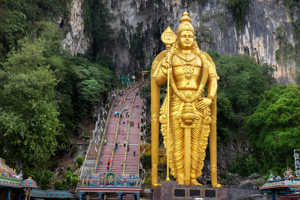 Gouden Murugan-beeld bij de Batu Caves met kleurrijke trap tegen kalkstenen rotswand, nabij Kuala Lumpur, Maleisië.