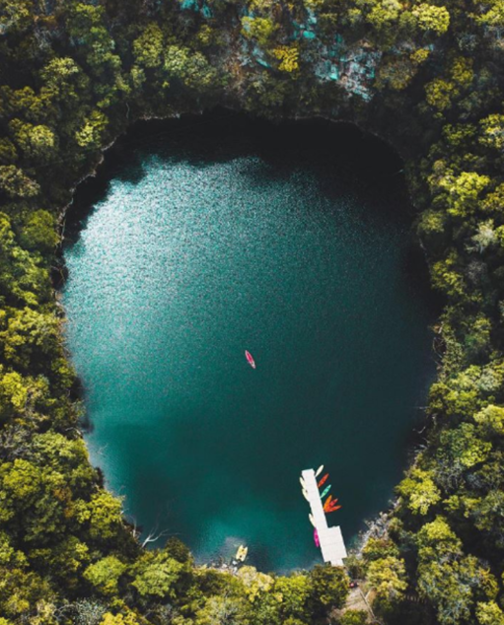 Bovenaanzicht van een helderblauw meer in de jungle van Mexico met kano’s aan een steiger.