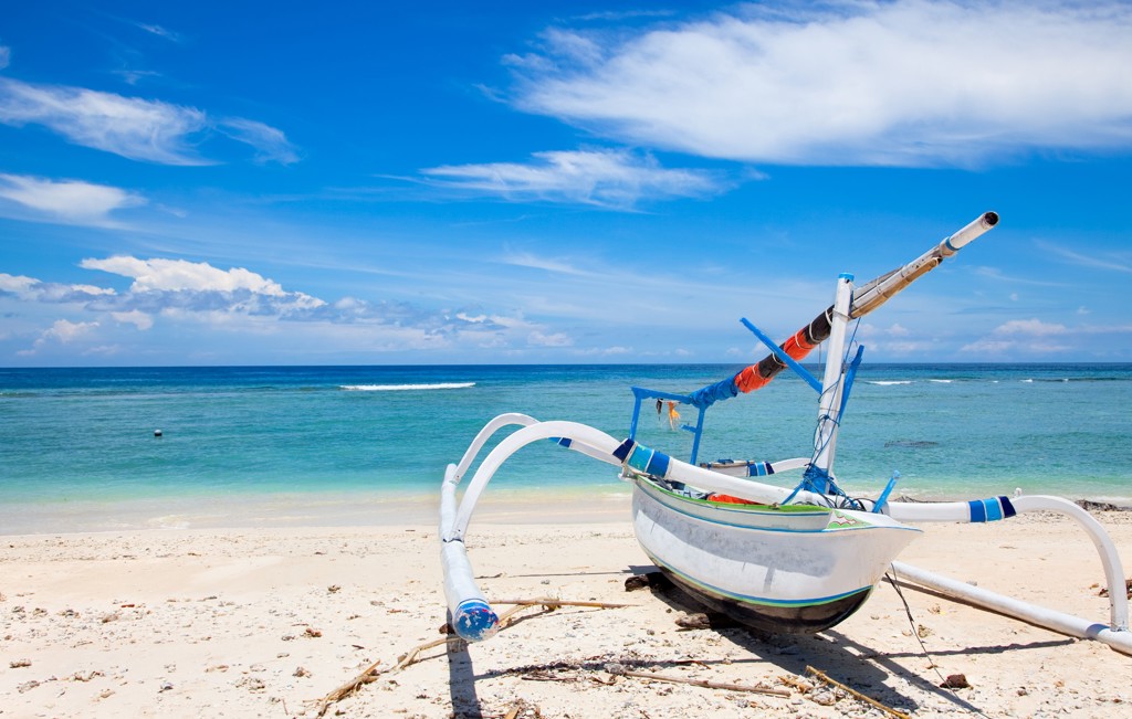 Traditionele vissersboot op het witte strand van Bali met turquoise zee en blauwe lucht.