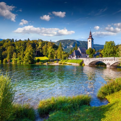 Kerk en stenen brug bij het Meer van Bled in Slovenië, omringd door bergen en bos.