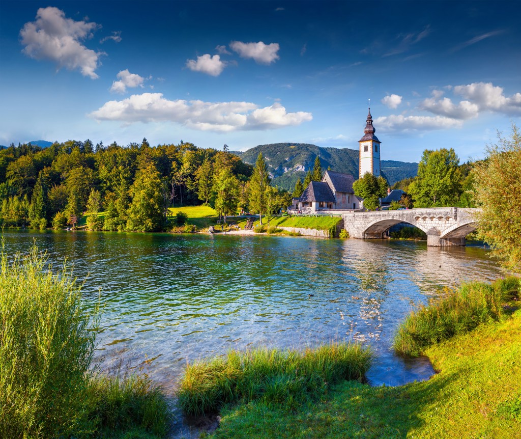Kerk en stenen brug bij het Meer van Bled in Slovenië, omringd door bergen en bos.
