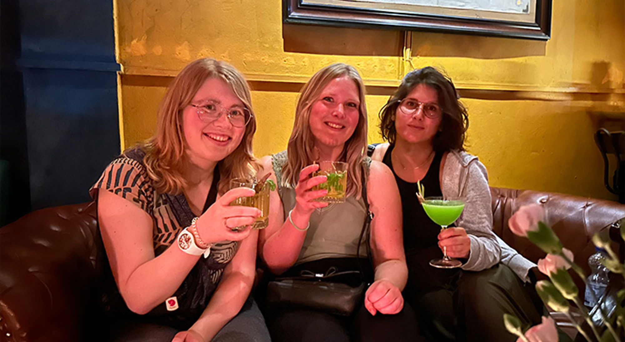 Nieuwe vrienden Vrienden proosten met cocktails op een leren bank in een gezellige bar.