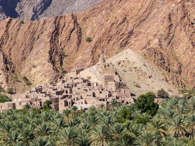 Traditioneel lemen dorp in Oman aan de voet van ruige bergen, met palmoase op de voorgrond.