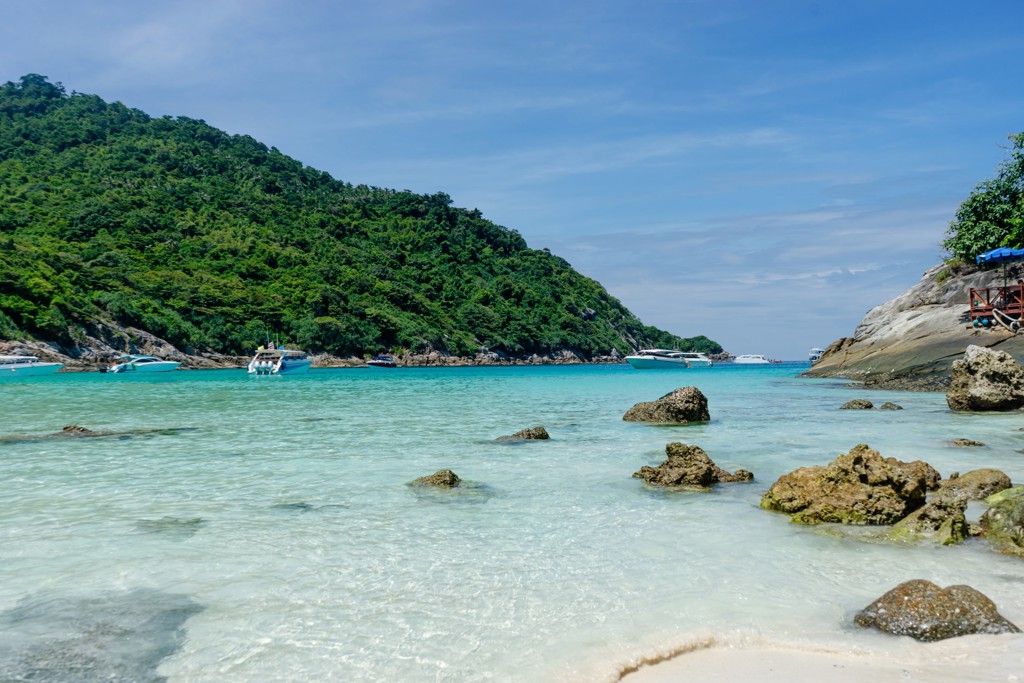 Tropisch strand in Thailand met helderblauw water, rotsen en boten voor de kust.