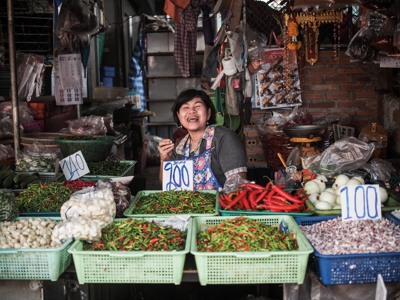 Vrolijke marktverkoper op een Thaise markt met bakken rode en groene pepers, knoflook en uien.
