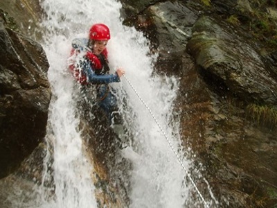 Canyoning in de Écrins: deelnemer met helm daalt langs een waterval af aan een touw.