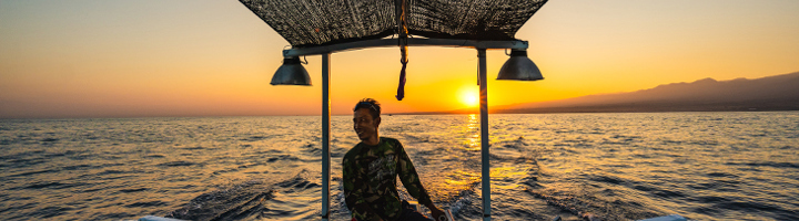 Man op een boot bij zonsondergang op zee in Indonesië.