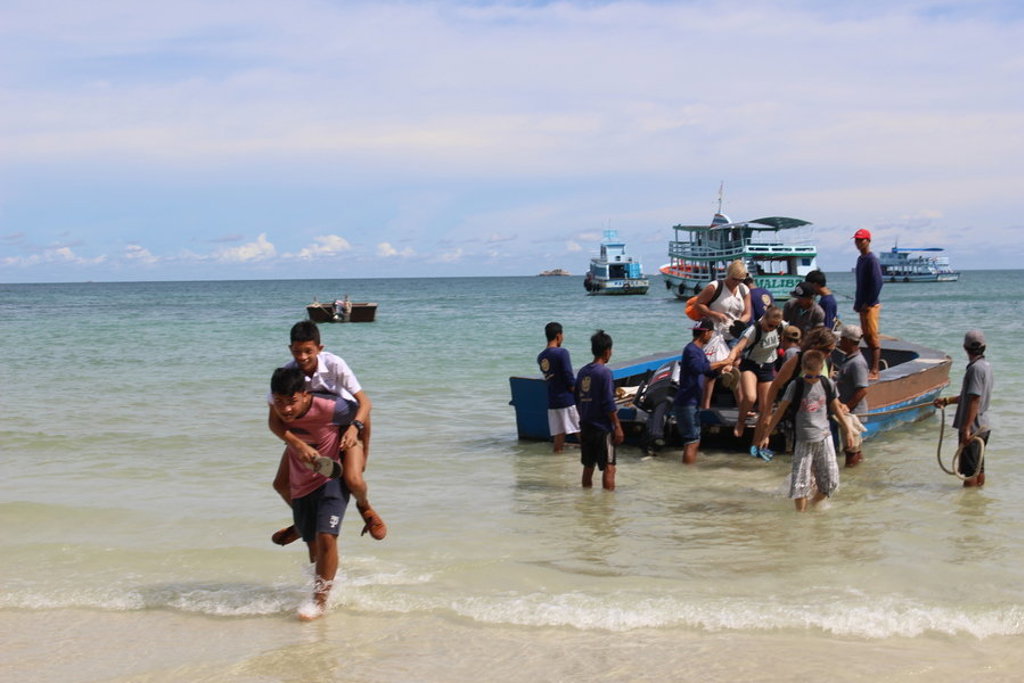 Gezin stapt vanaf een longtailboot het strand op in Thailand tijdens een familiereis.