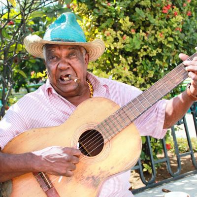 Straatmuzikant in Havana speelt gitaar en rookt een sigaar.