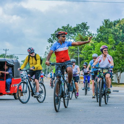 Groep fietsers tijdens fietsvakantie in Sri Lanka, met lokale tuktuk op de weg.