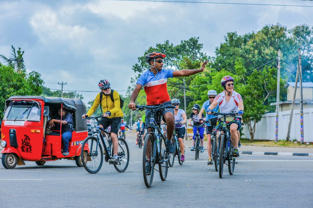 Groep fietsers tijdens fietsvakantie in Sri Lanka, met lokale tuktuk op de weg.