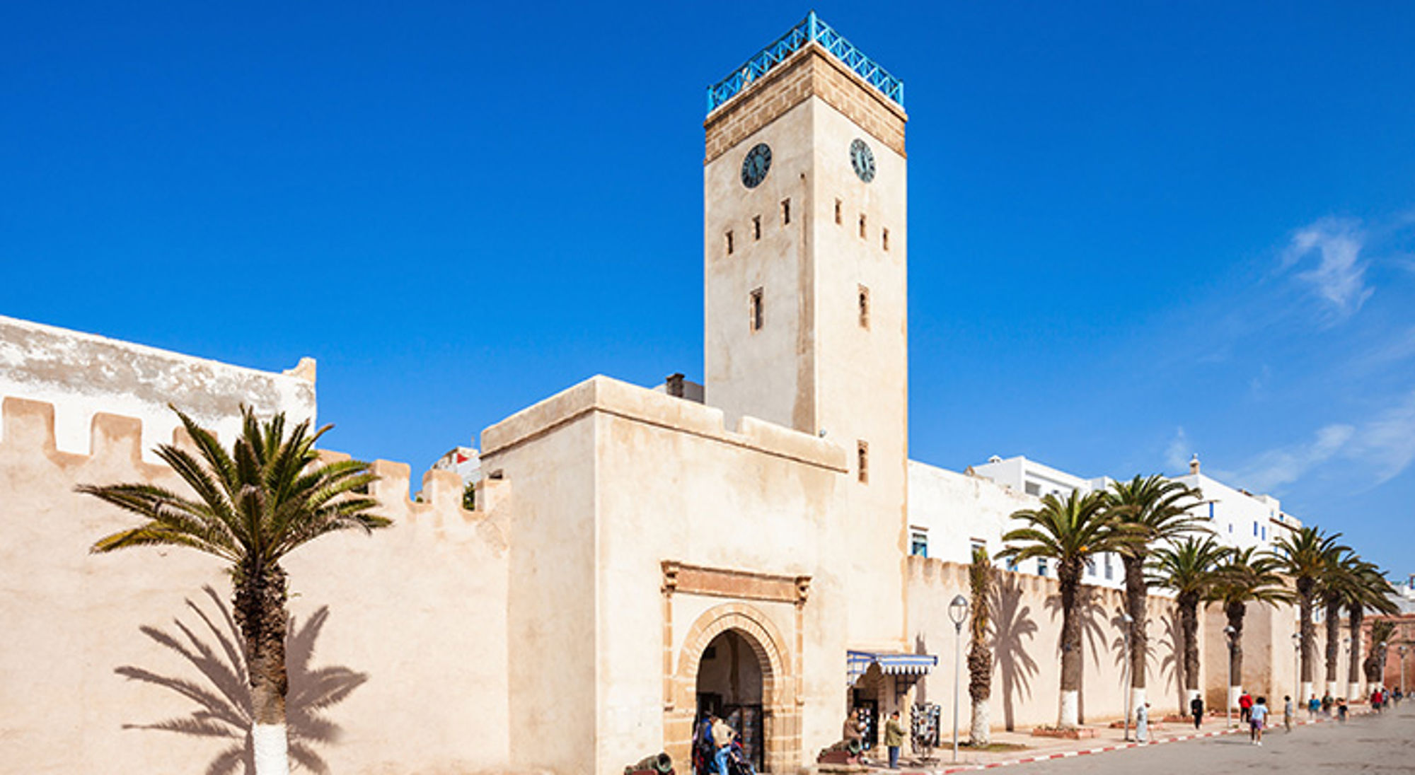 Clock tower Essaouira Witte stadsmuur met klokkentoren en palmbomen in Marokko onder een heldere blauwe lucht.