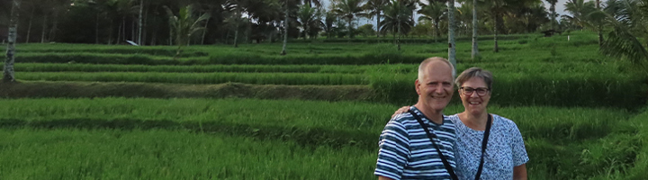 Carin en Theo in de rijstvelden van Indonesië, met palmbomen op de achtergrond.