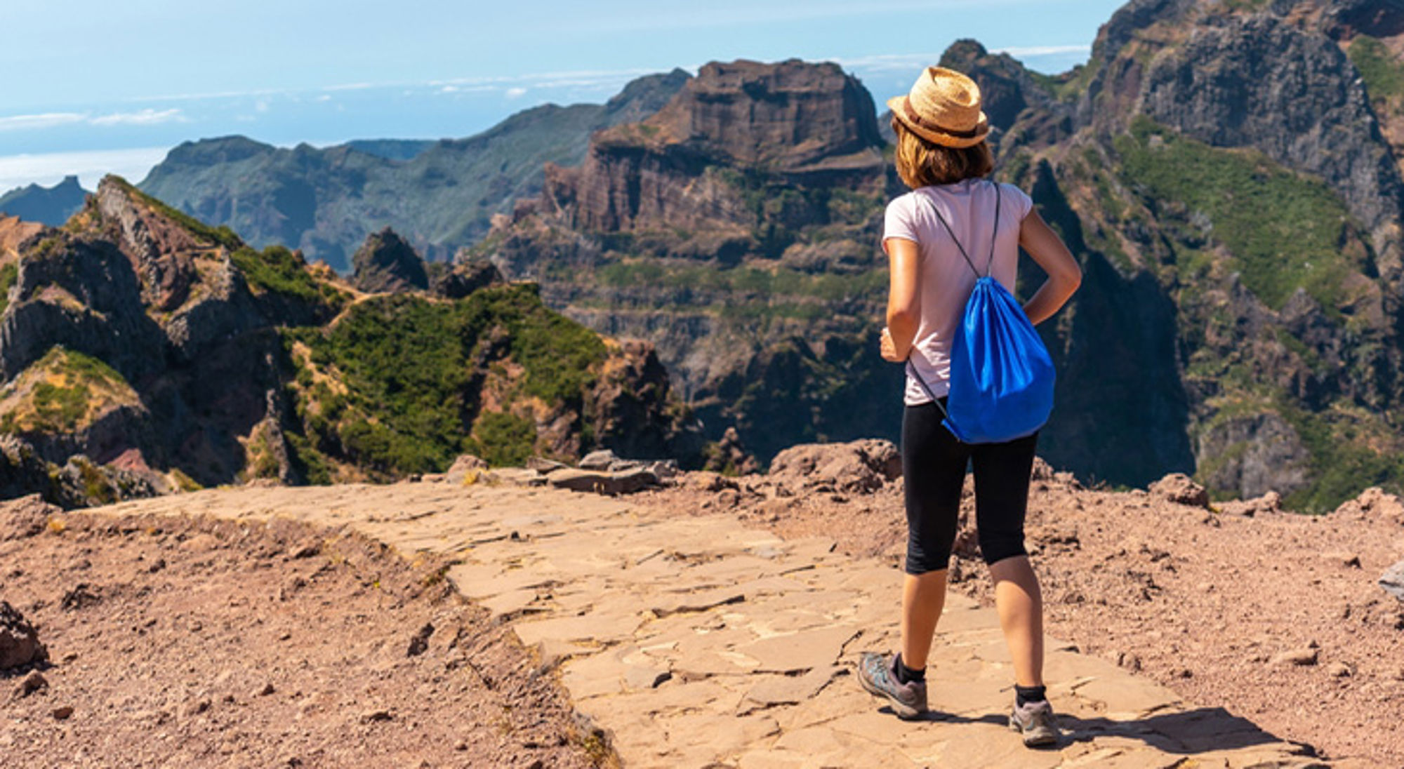 Wandelen Madeira Wandelaar met rugzak kijkt uit over ruige bergkliffen en groene valleien tijdens een hike.