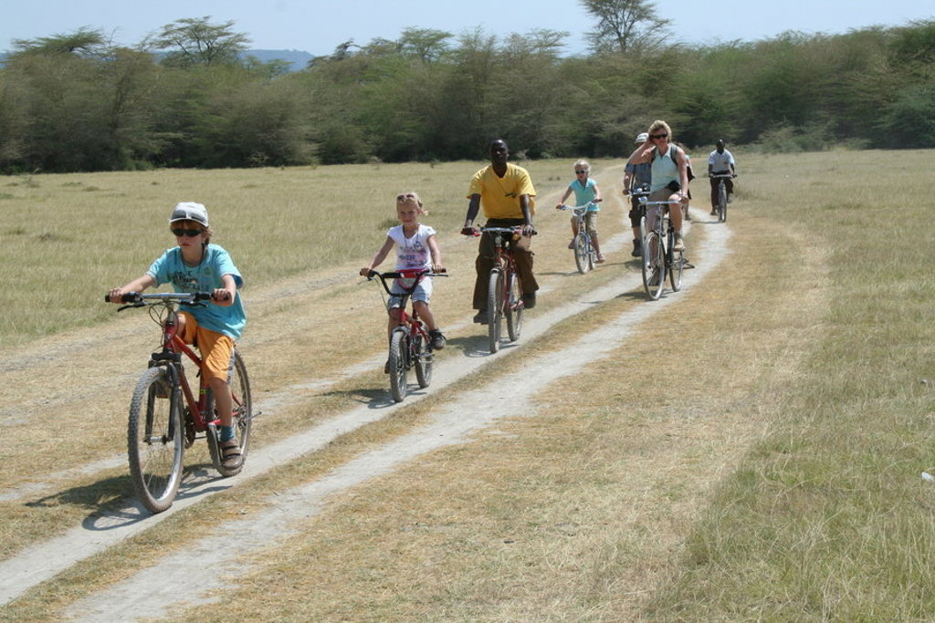 Gezin fietst over een zandpad door de Tanzaniaanse savanne tijdens familiereis Tanzania en Zanzibar.