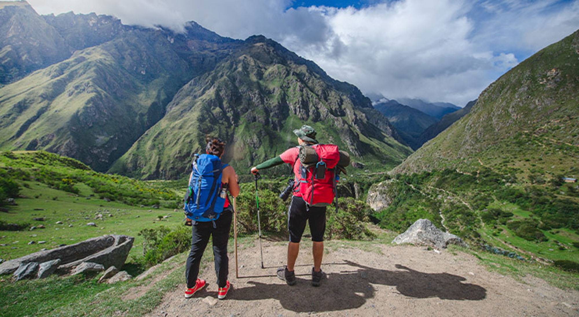 Inca Trail Twee wandelaars met rugzakken kijken uit over een groene bergvallei tijdens een trekking.