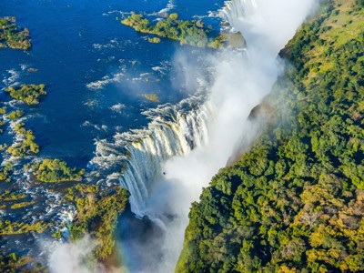 de Victoria Falls met nevel boven de Zambezi-rivier en groene oevers.
