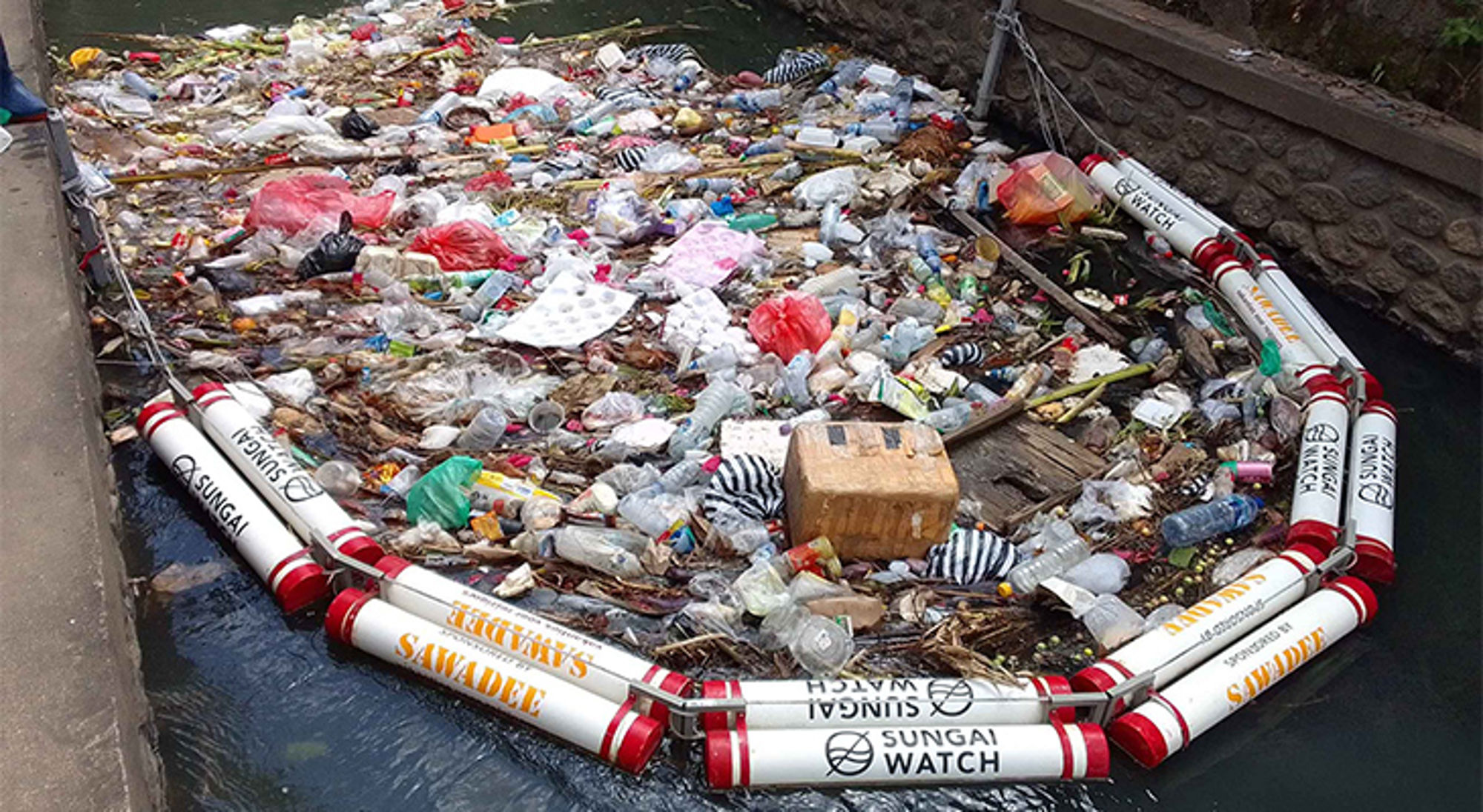 Sawadee afvalbarrière Drijvend afval en plastic flessen in een rivier, tegengehouden door een drijvende barrière.