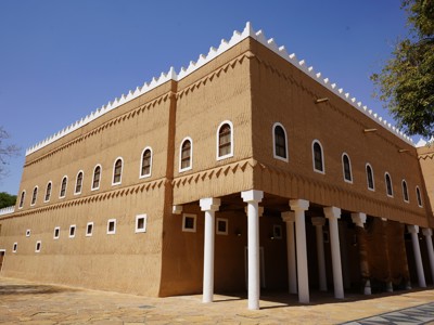 Traditioneel lemen fort in Saoedi-Arabië met witte kantelen en zuilengalerij onder een heldere blauwe lucht.