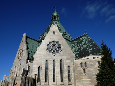 Basiliek Sainte-Anne-de-Beaupré in Quebec met groen koperen dak en roosvenster tegen blauwe lucht.