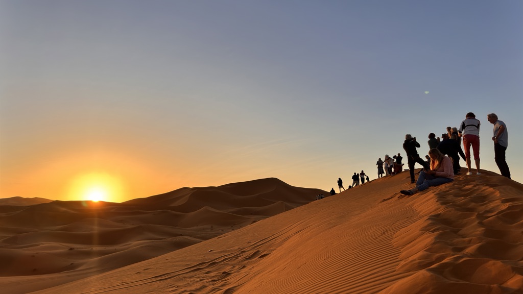 Zonsondergang in de Marokkaanse woestijn met reizigers op een zandduin tijdens een familiereis Marokko.