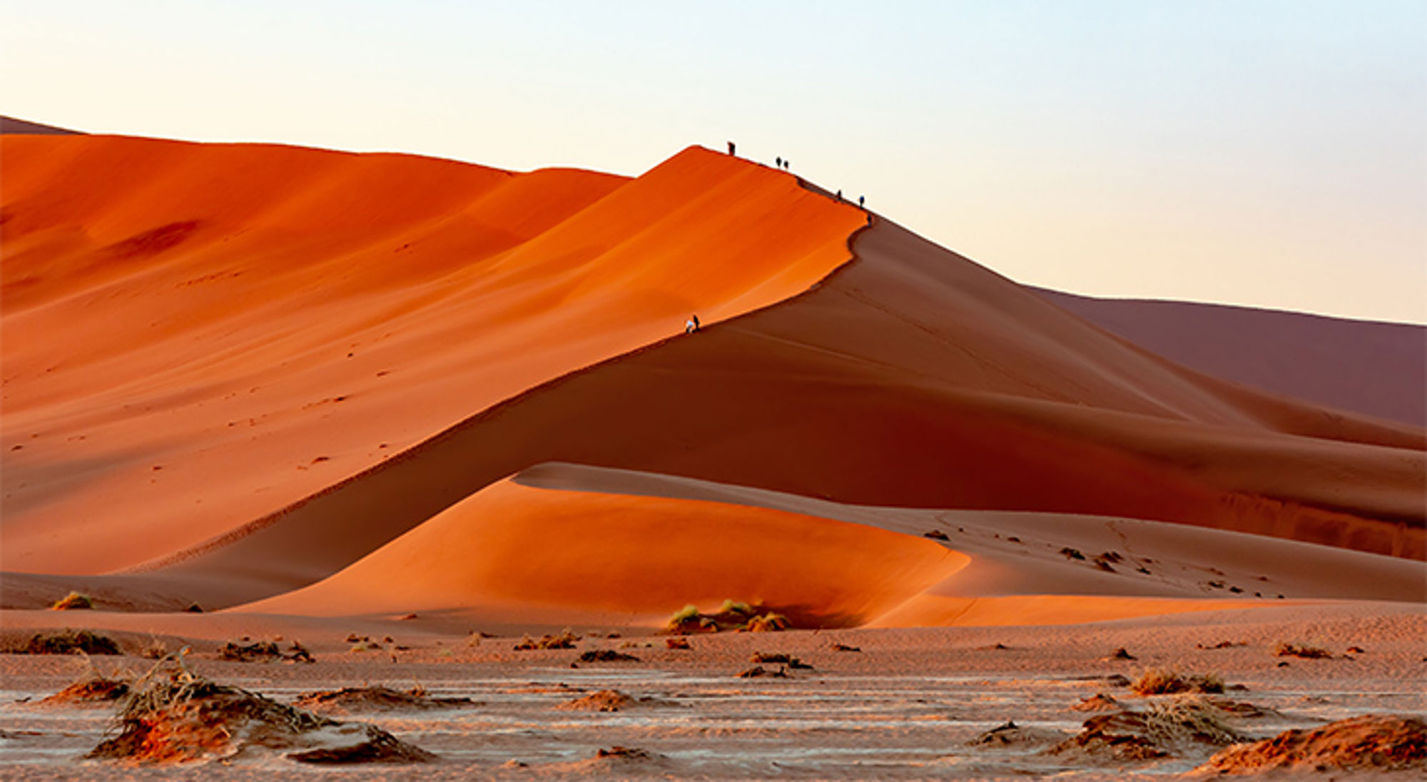 Sossusvlei Namibië Oranje zandduinen in de woestijn bij zonsondergang, met wandelaars op de kam.