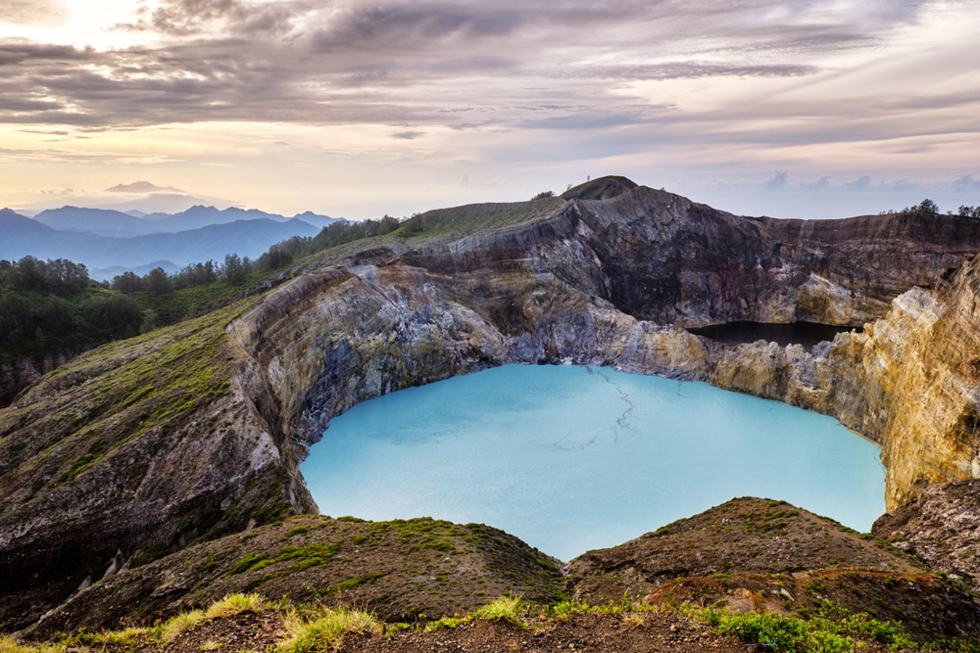 Turquoise kratermeer van de Kelimutu-vulkaan op Flores, Indonesië, met ruige rotswanden en bergen.