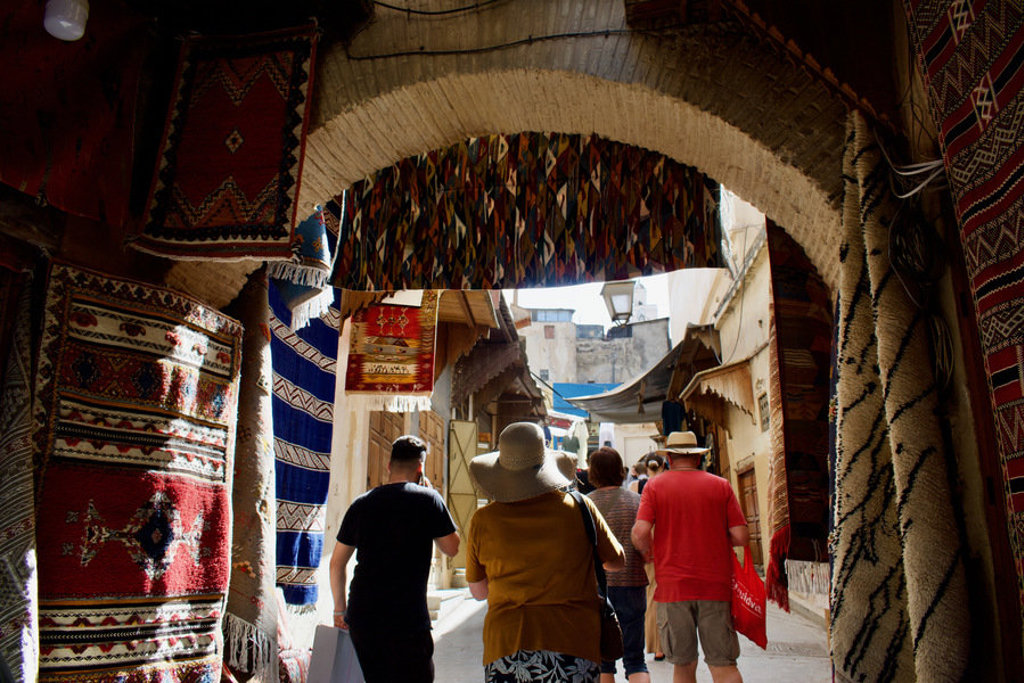 Reizigers lopen door een souk in Marokko langs kleurrijke tapijten tijdens de groepsrondreis Marokko Premium.