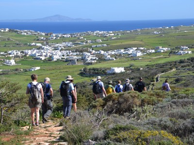 Wandelaars met rugzakken dalen af op Naxos met uitzicht op witte dorpjes, groene velden en de Egeïsche Zee.