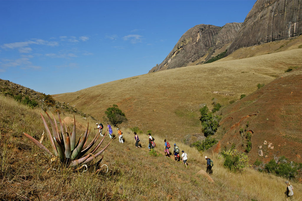 Wandelaars tijdens groepsrondreis Madagascar in berglandschap met rotswanden en savanneheuvels.